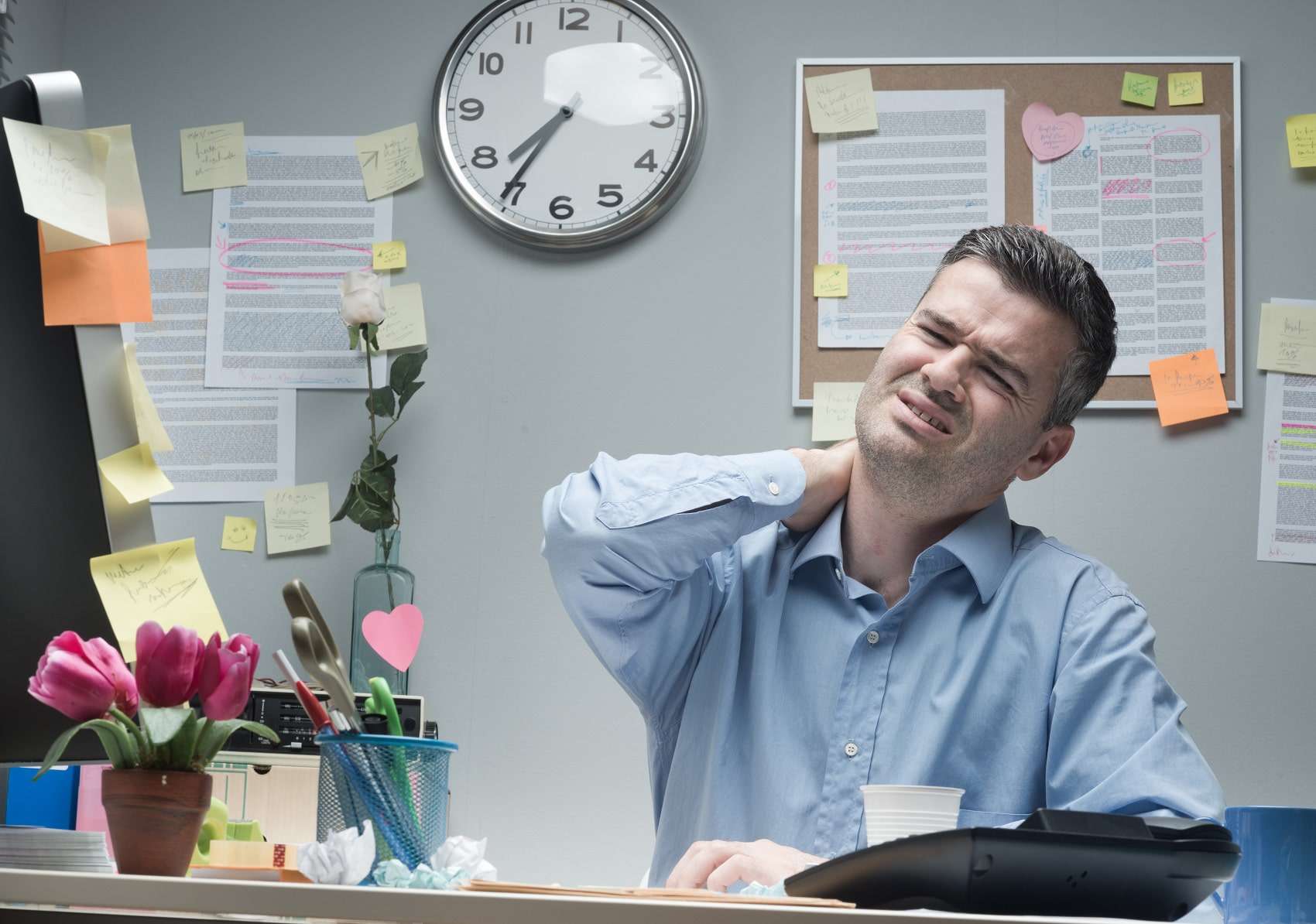Tired businessman with forward head posture, sitting at desk touching his painful neck