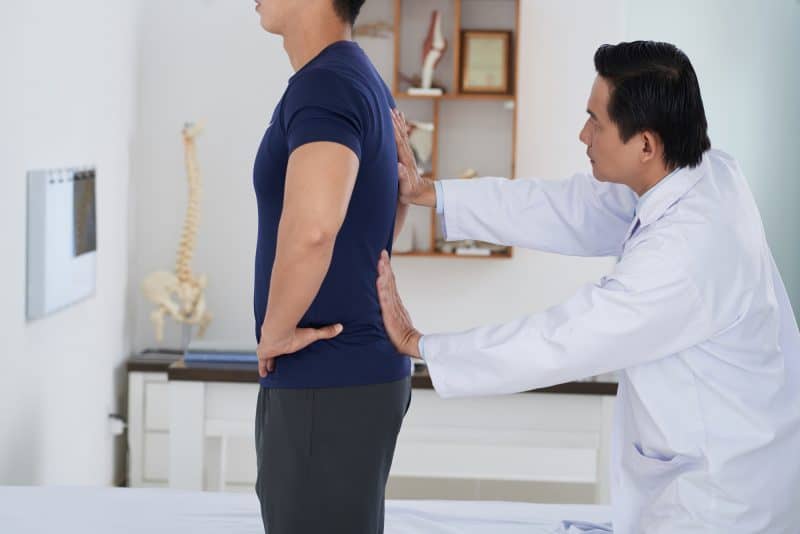 Vietnamese sports doctor examining spine of young patient