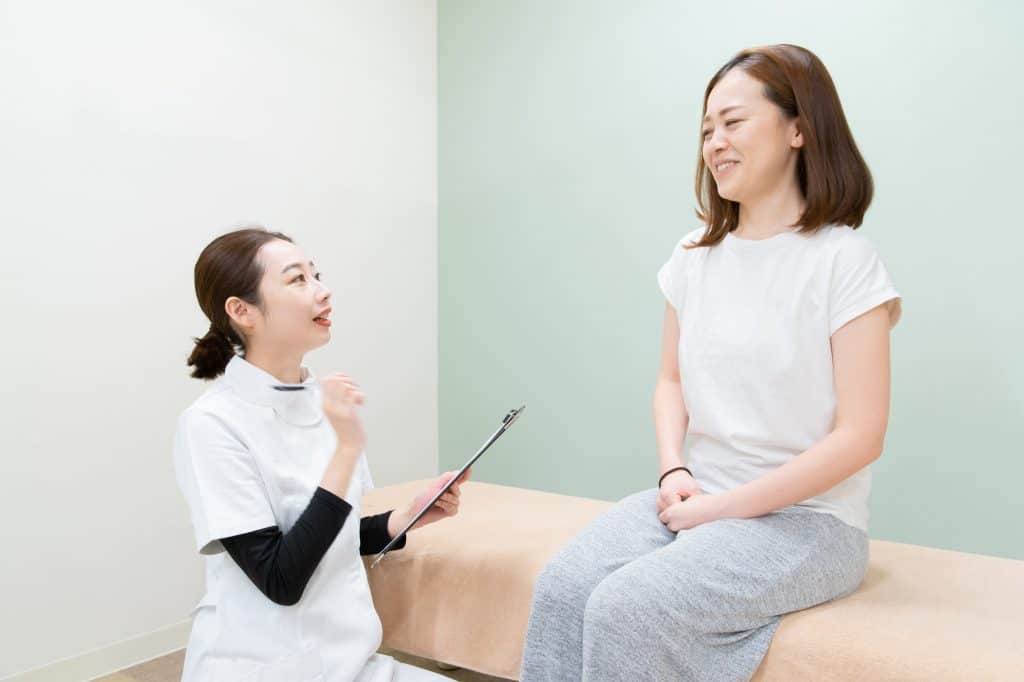 Asian female practitioner listening to female patient's symptom and explaining treatment method