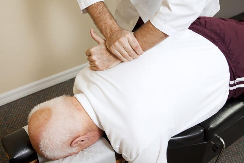 Closeup of chiropractors hands doing spinal adjustment on senior man.